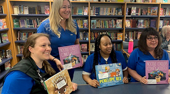 Four nurses holding books while seated in a library common area.